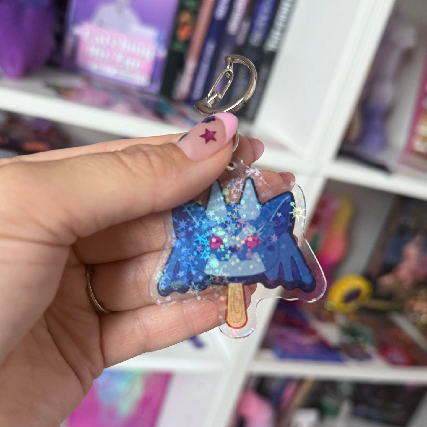 Hand holding a blue gargoyle-shaped keychain with colorful details against a blurred store background.